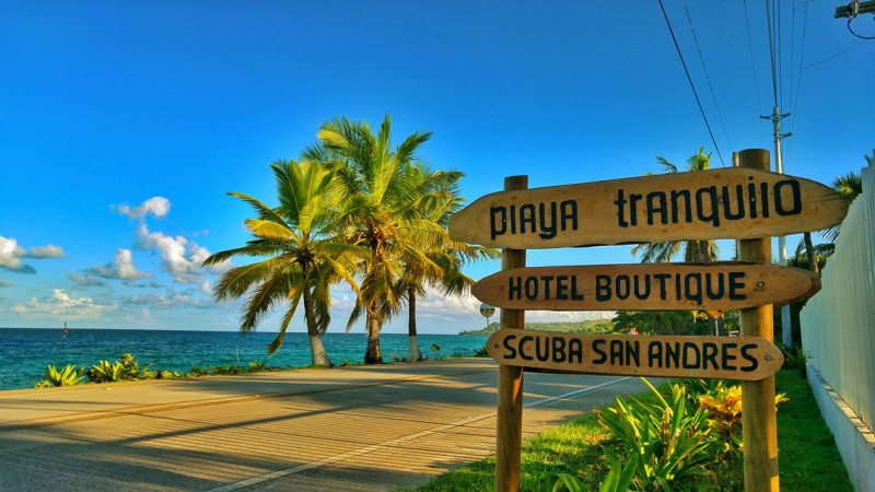 Placa do Hotel Boutique Playa Tranquilo, com mar e palmeiras ao fundo.