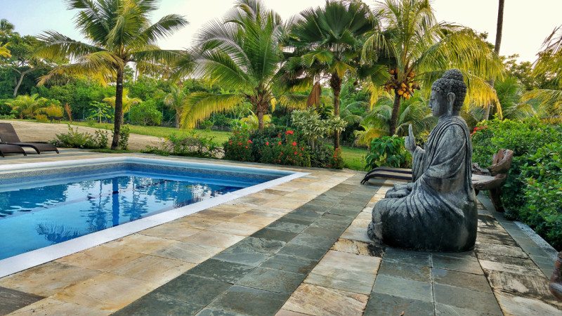 Vista da piscina do hotel, com estátua de Buda e área verde em volta.