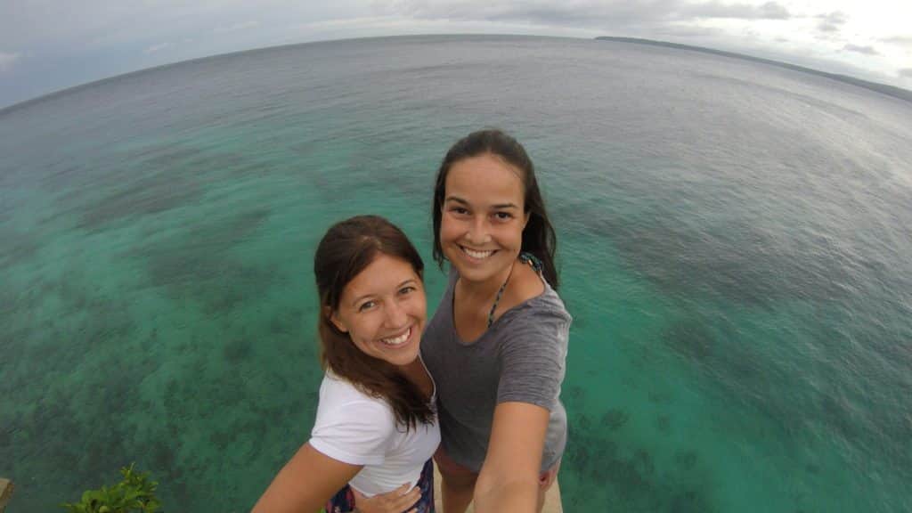 Duas mulheres brancas estão na beira de alguma superfície tirando uma selfie com uma vista ampla do oceano e um céu nublado ao fundo na praia de Salagdoong. Representa o post sobre melhores praias nas Filipinas.