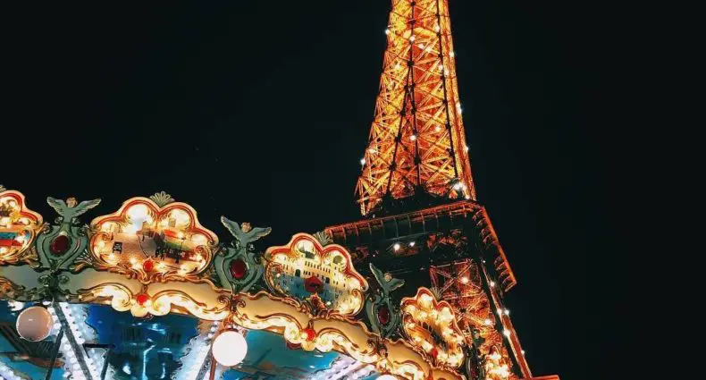 Visão de baixo do carrossel que fica próximo à Torre Eiffel, uma das opções de o que fazer em Paris. As duas atrações estão iluminadas contra o céu noturno.