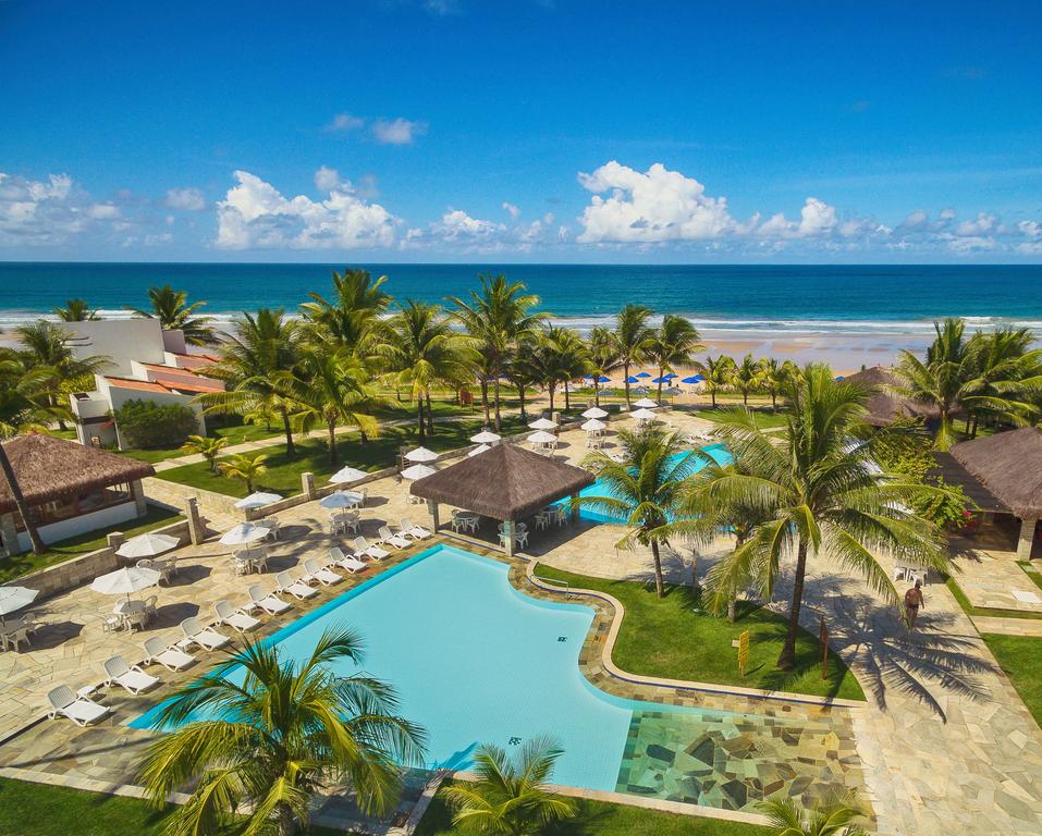 Áreas com piscinas do Hotel Village, com coqueiros em volta e uma praia ao fundo