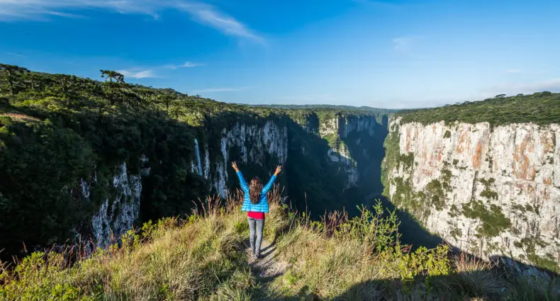 Uma pessoa no topo da montanha com os braços abertos admirando as outras montanhas. Imagem para ilustrar post sobre o que fazer em Cambará do Sul.