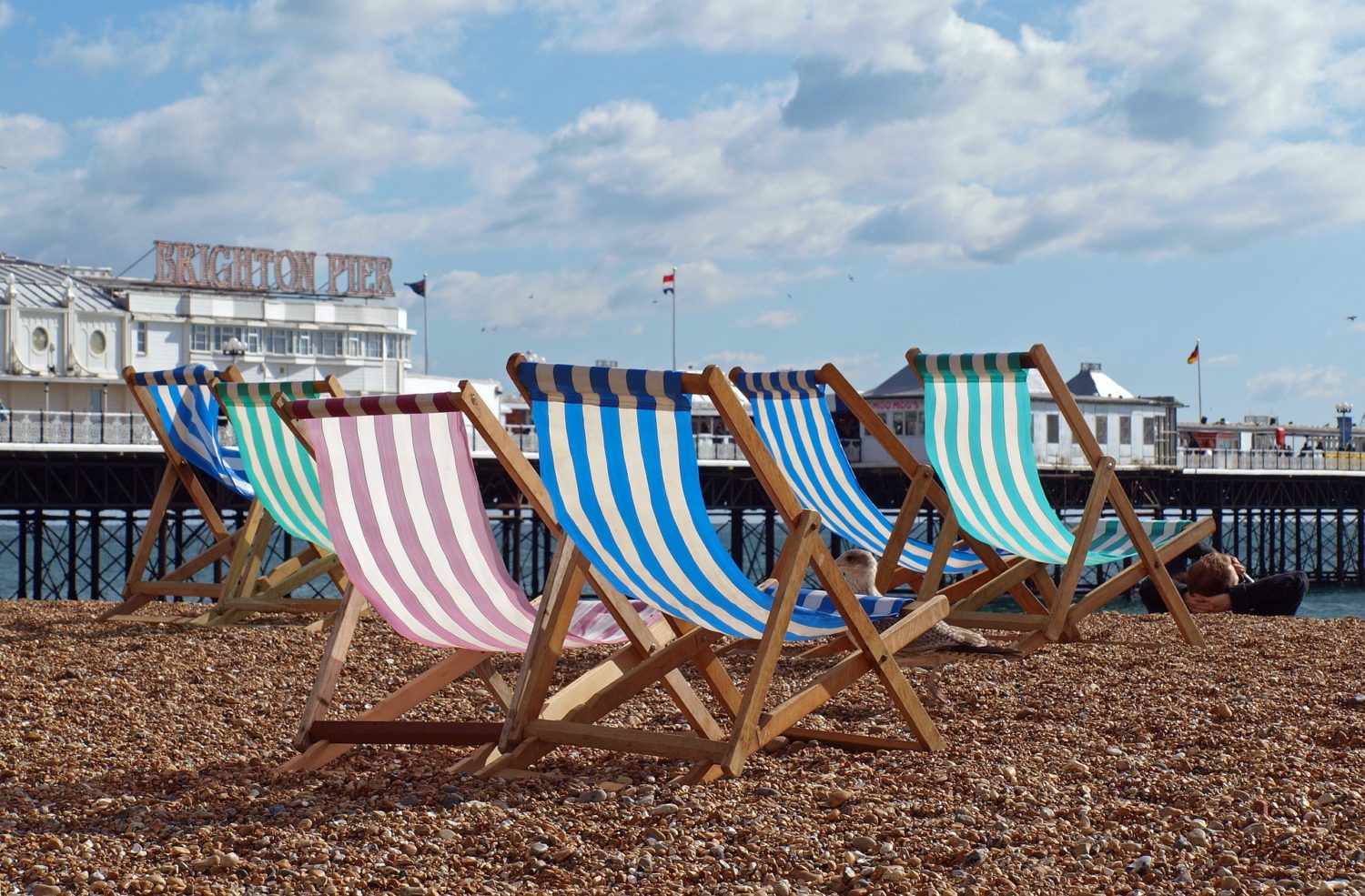 Vista de praia em Brighton com cadeiras e pier ao fundo. Foto de Willi Heidelbach via Pixabay.