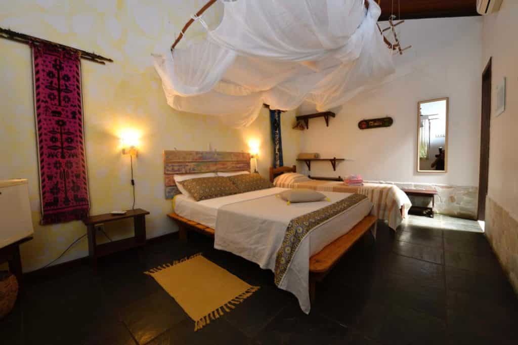 Um quarto da Pousada Horizonte Azul com duas camas, mosquiteiros, decorações de parede, um espelho e uma pequena mesa com toalhas.