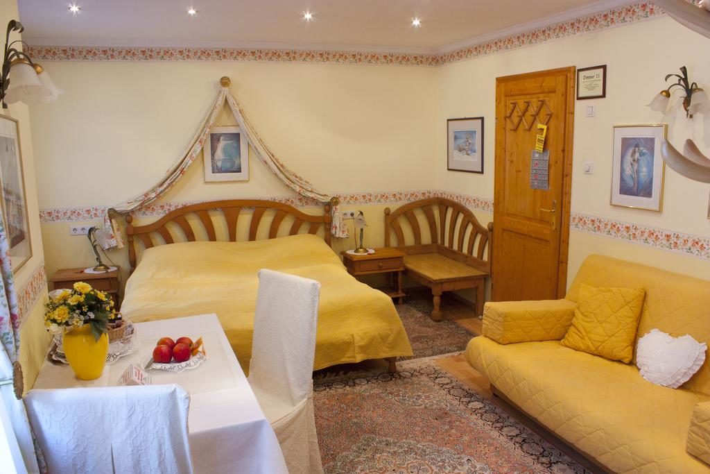 Quarto do Hotel Schneider-Gössl, com cama, mesa com vaso de flores e frutas, cadeiras, sofás e ambiente caseiro.