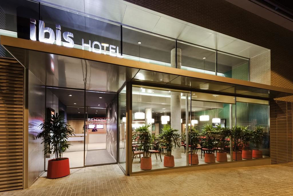 Fachada do Ibis Barcelona Centro, uma das recomendações de hotéis baratos em Barcelona.  A entrada é feita de vidro com o nome do hotel em cima, e há plantas por toda a extensão.