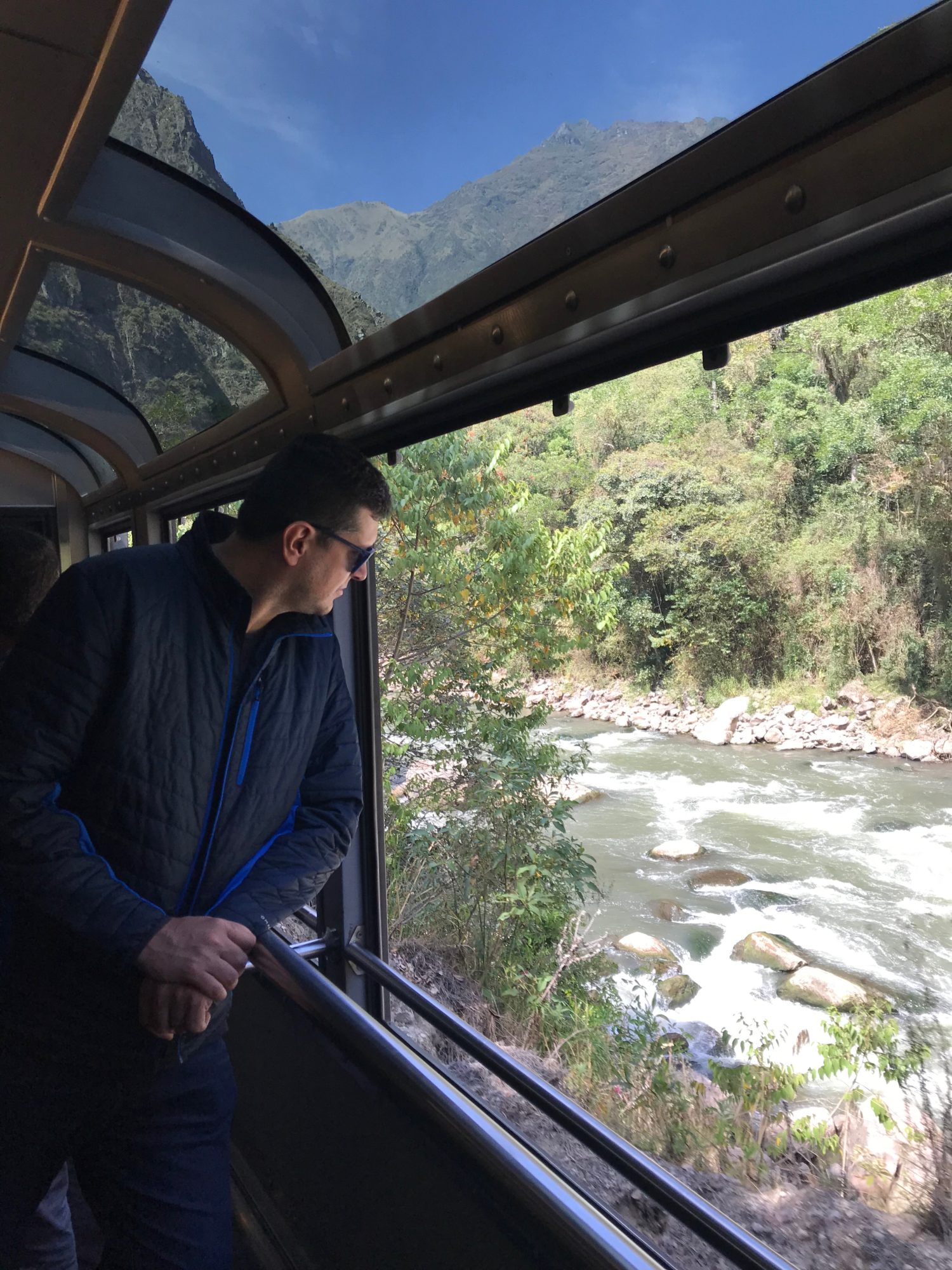 Foto de Flávio Antunes no trem aberto do vagão 360, com vista panorâmica da paisagem entre Cusco e Machu Picchu