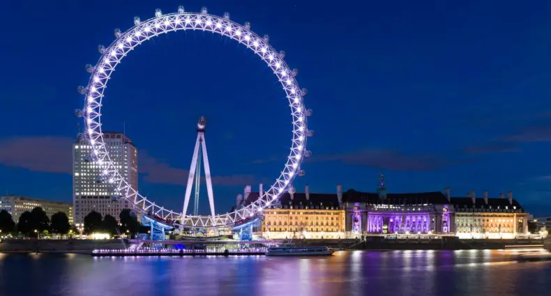 Vista da London Eye, em Londres, com luzes acesas e céu azul escuro ao fundo.