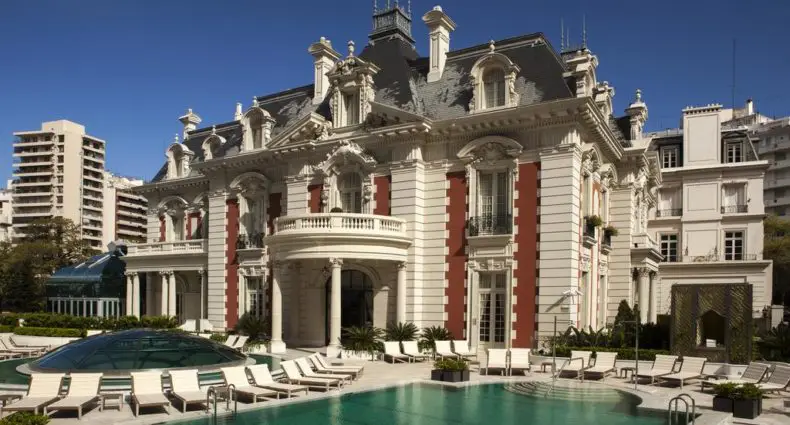 Four Seasons Hotel em Buenos Aires, em estilo de mansão com arquitetura ornamentada, piscina externa, espreguiçadeiras e prédios altos ao fundo, para representar melhores hotéis em Buenos Aires.