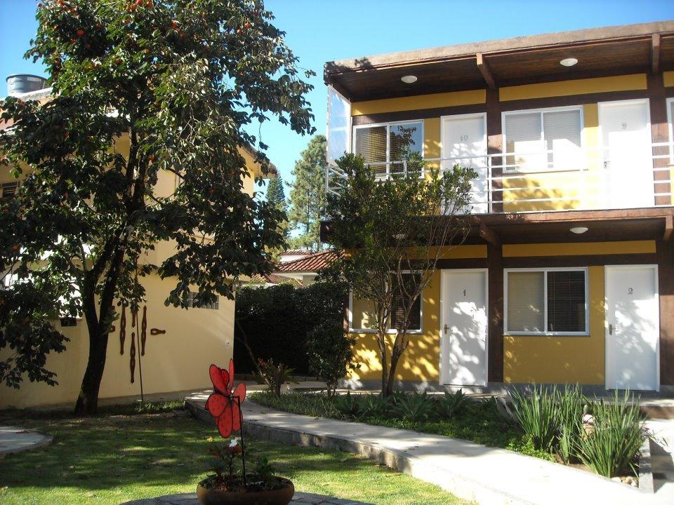 Pousada HospedaBia com casa em tom amarelo, marrom e portas brancas e gramado e árvores verdes, ilustrando post pousadas em Teresópolis.