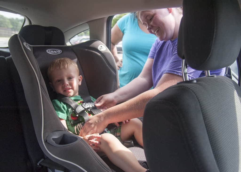Criança sendo arrumada em cadeirinha de carro, exigência nos Estados Unidos