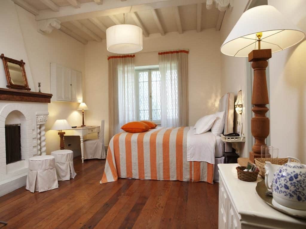 Quarto com decoração retrô e estilosa no Quinta Miraflores, com cama alta, lençóis listrados, abajur, bule de porcelada, lareira de gesso, escrivaninha e cortinas.