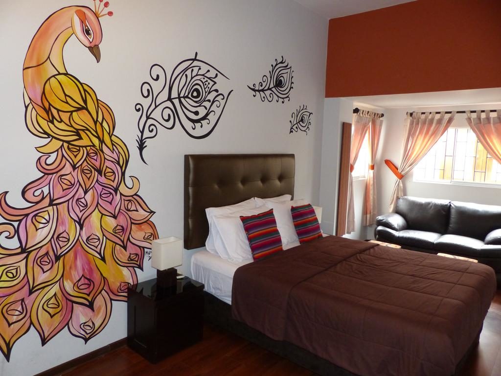 Quarto no The Lighthouse Bed & Breakfast, uma alternativa aos hotéis em Lima, com cama de casal, sofá, e pintura de pavão colorido em tons de laranja na parede ao lado da cama