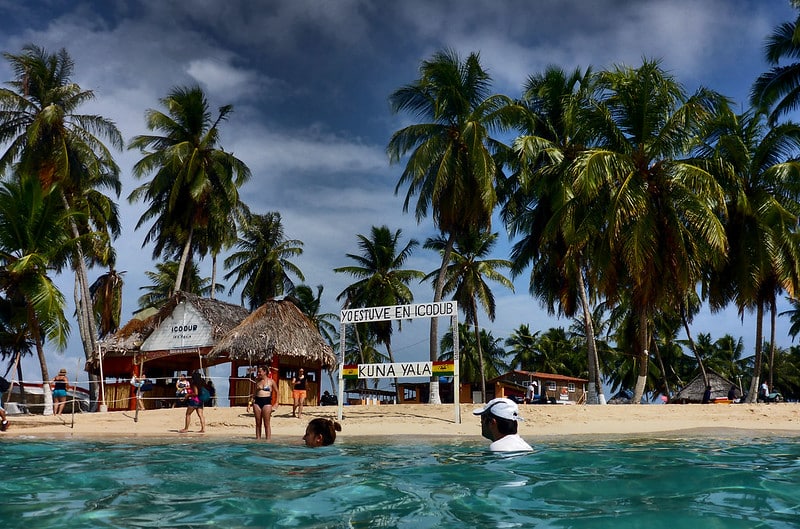 Foto de beira da praia com cabanas e palmeiras na Isla Aguja, uma das ilhas de San Blas