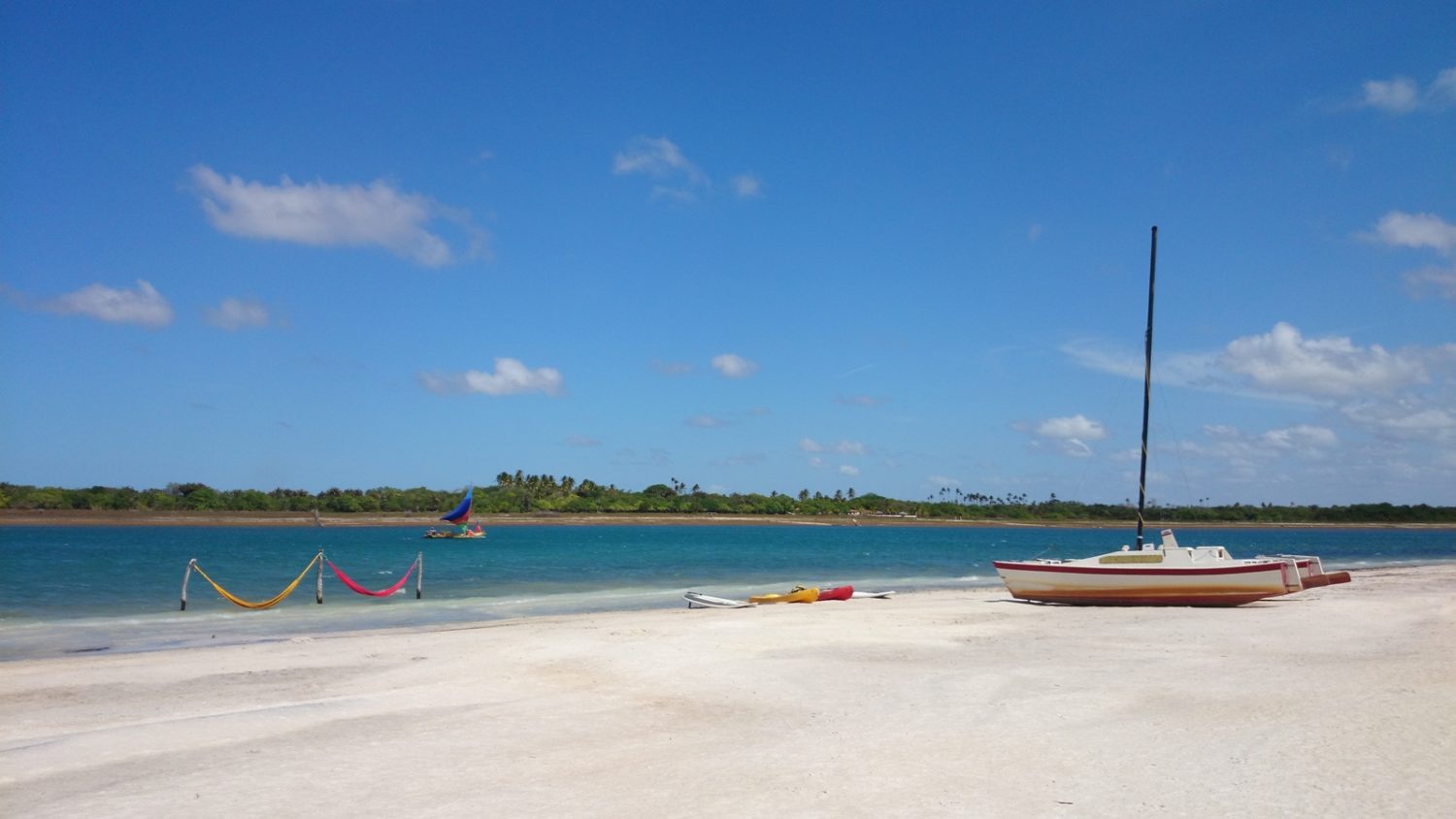 Jericoacoara, no Ceará, com praia de areia clara e mar azul turquesa, barco em dia de céu limpo e sol