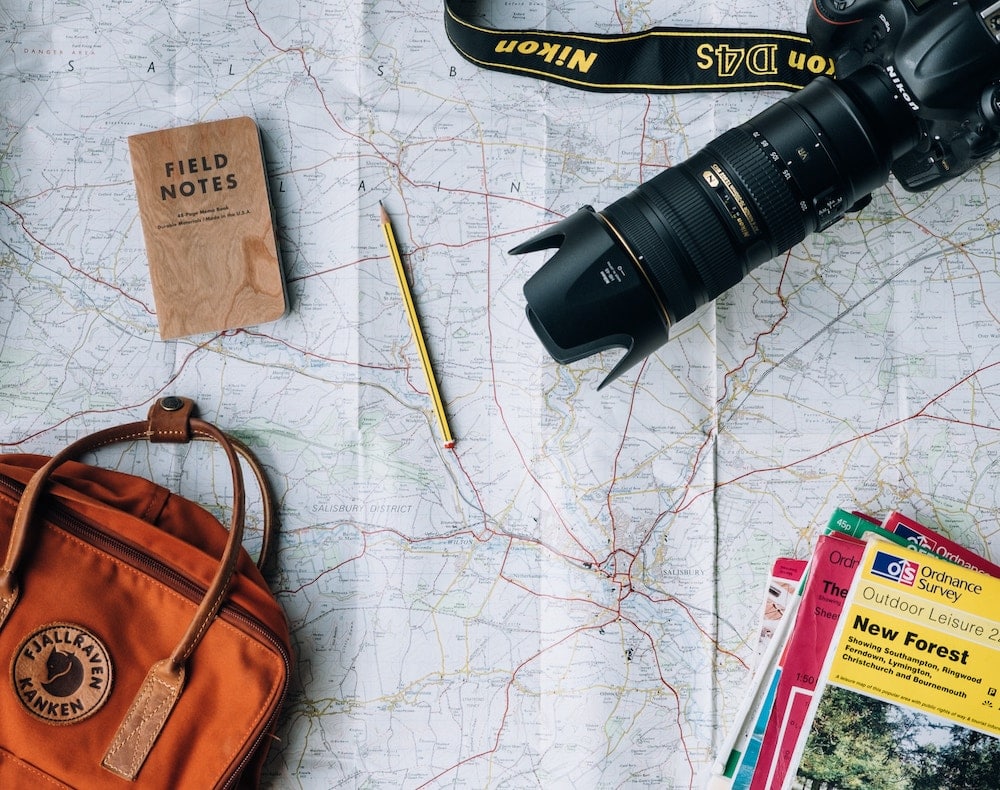 mapa com uma câmera nikon, um caderno de notas, um lápis, uma mochila e alguns livros de turismo