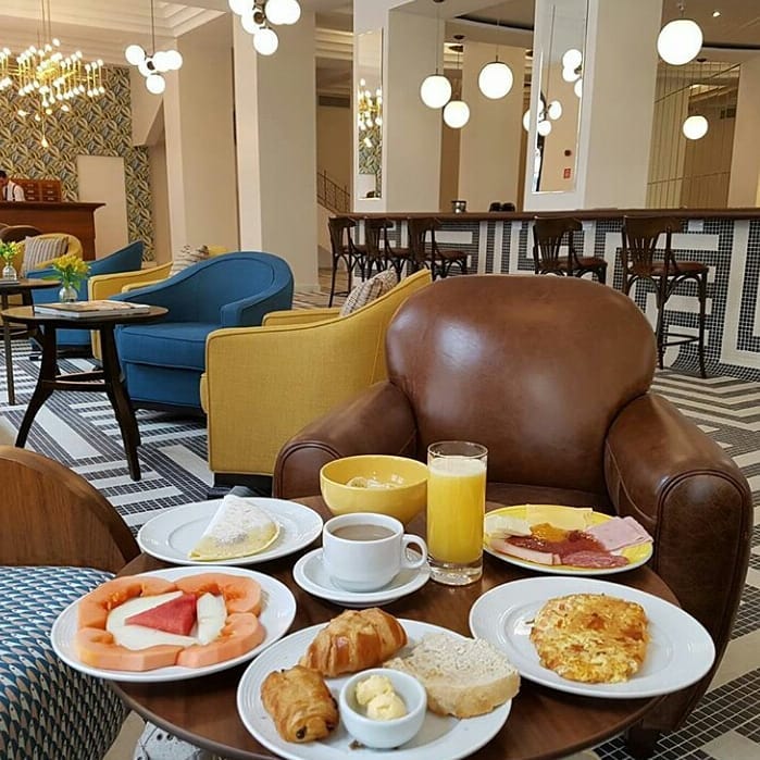 Mesinha do restaurante do hotel com pratos com alimentos de café da manhã como croissant, pães, frutas, tapioca, suco e café com leite