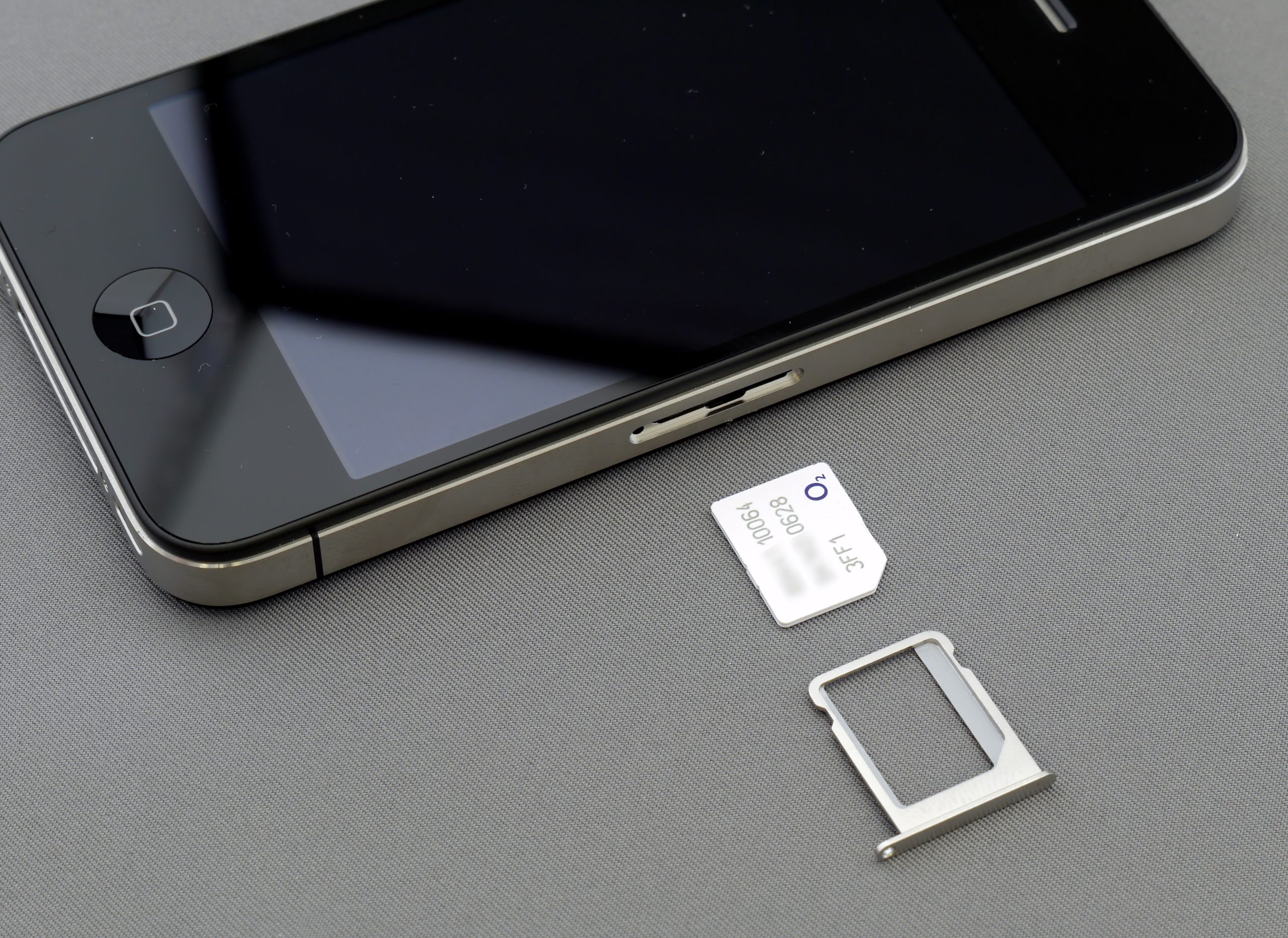 celular iphone preto deitado em cima de uma mesa cinza com um chip branco ao seu lado