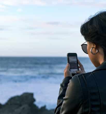 mulher fotografando com smartphone a praia do guincho em portugal