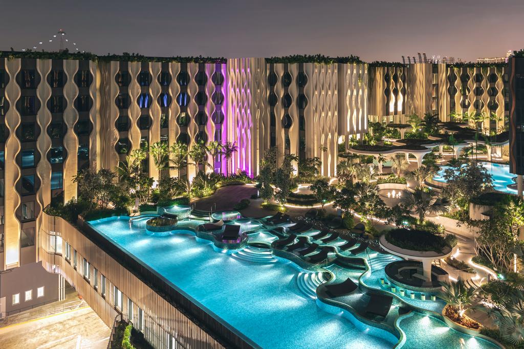 vista noturna do The Outpost Hotel Sentosa em Singapura com diversas piscinas iluminadas em frente as janelas dos quartos do hotel