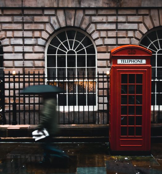 Londres em dia de chuva com pessoa andando ao lado de cabine vermelha de telefone