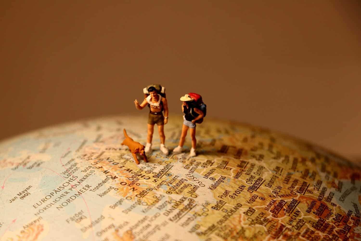 miniaturas de um homem, mulher e um cachorro viajando pelo globo do mapa mundi