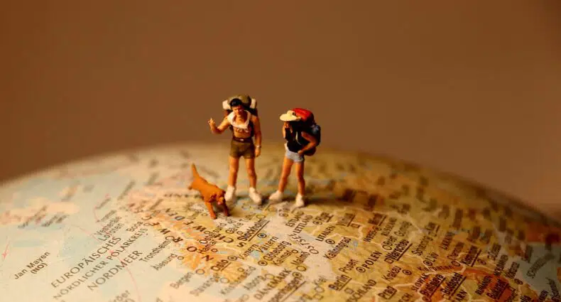 miniaturas de um homem, mulher e um cachorro viajando pelo globo do mapa mundi