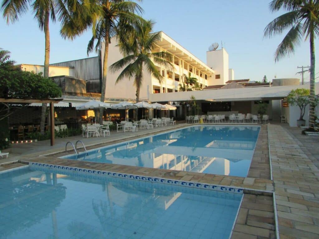 Piscinas do Ubatuba Palace Hotel, um dos hotéis em Ubatuba, com mesinhas, cadeiras e guarda-sóis ao fundo