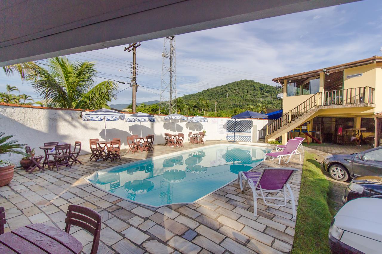 Piscina da Viamar Pousada com espreguiçadeiras e mesas em um pátio de azulejos, cercada por um muro, com uma casa e uma colina ao fundo.
