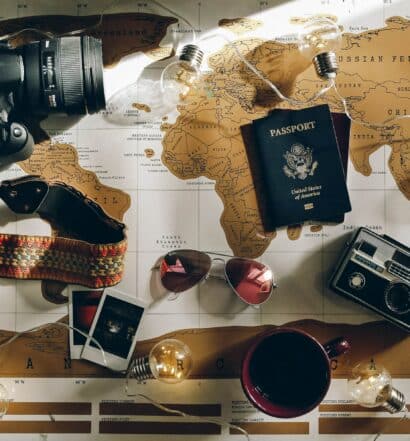 mapa mundi com uma câmera, um óculos de sol, passaporte, café e fotos em cima para representar o seguro saúde viagem