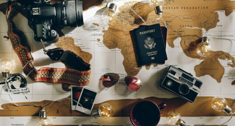 mapa mundi com uma câmera, um óculos de sol, passaporte, café e fotos em cima para representar o seguro saúde viagem