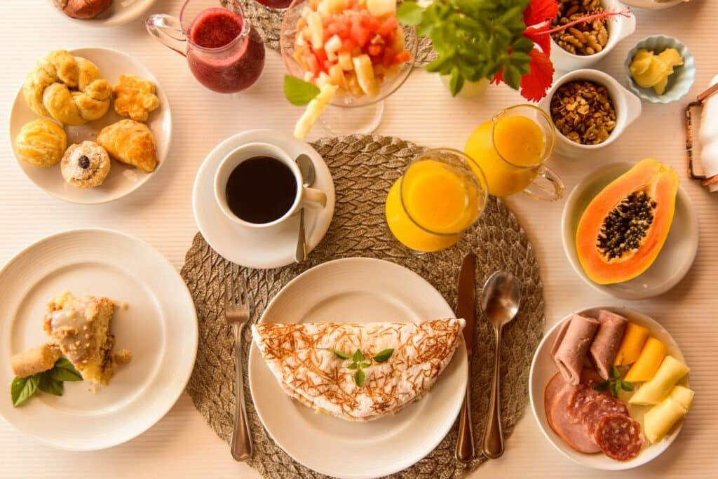 Café da manhã da Pousada Corveta, em Fernando de Noronha, com tapioca, salgadinhos, xícara com café, copo com suco de laranja, uma metade de um mamão e um prato com frios