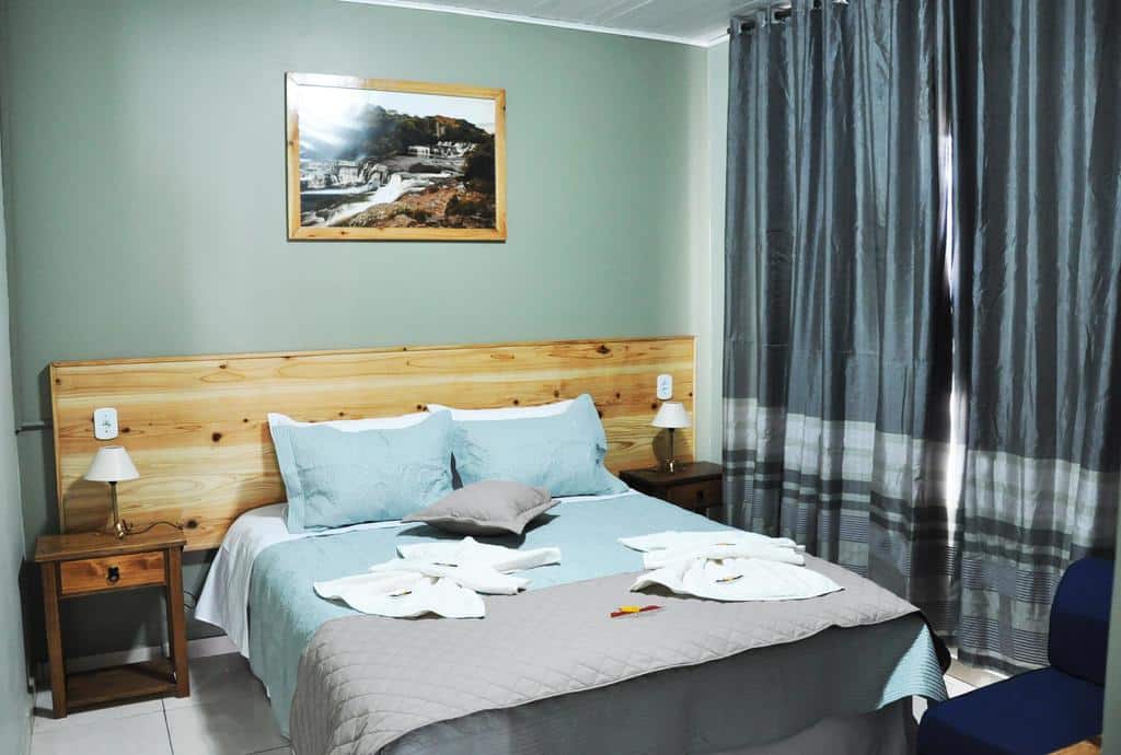 quarto da Pousada Encanto dos Cânions com uma cama de casal, duas cômodas e um quadro de cachoeira sobre a cabeceira