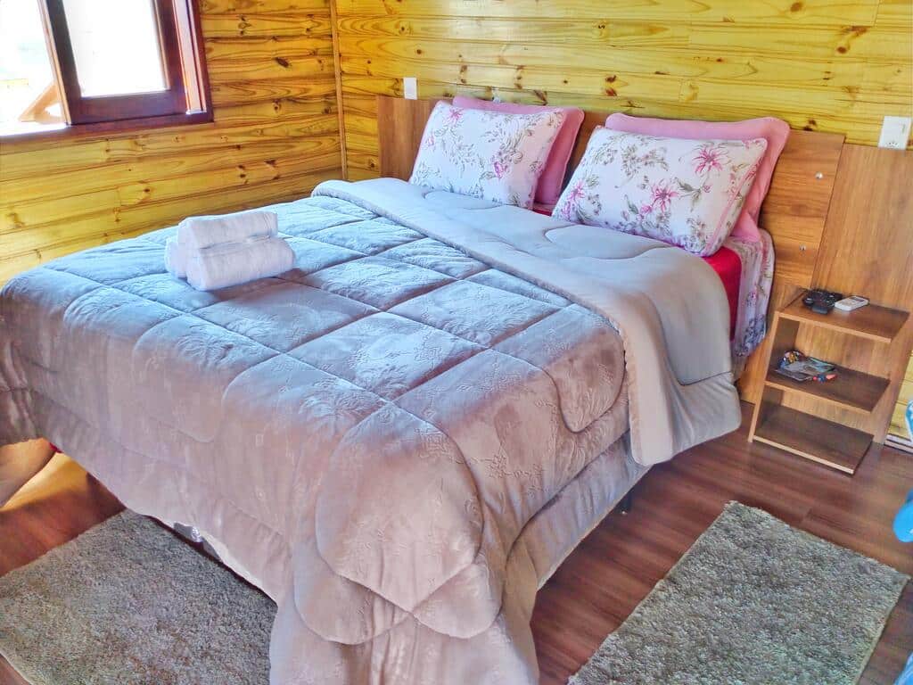 quarto da Pousada Bem Estar com uma cama de casal decorada com uma colcha e quatro travesseiros rosas e floridos