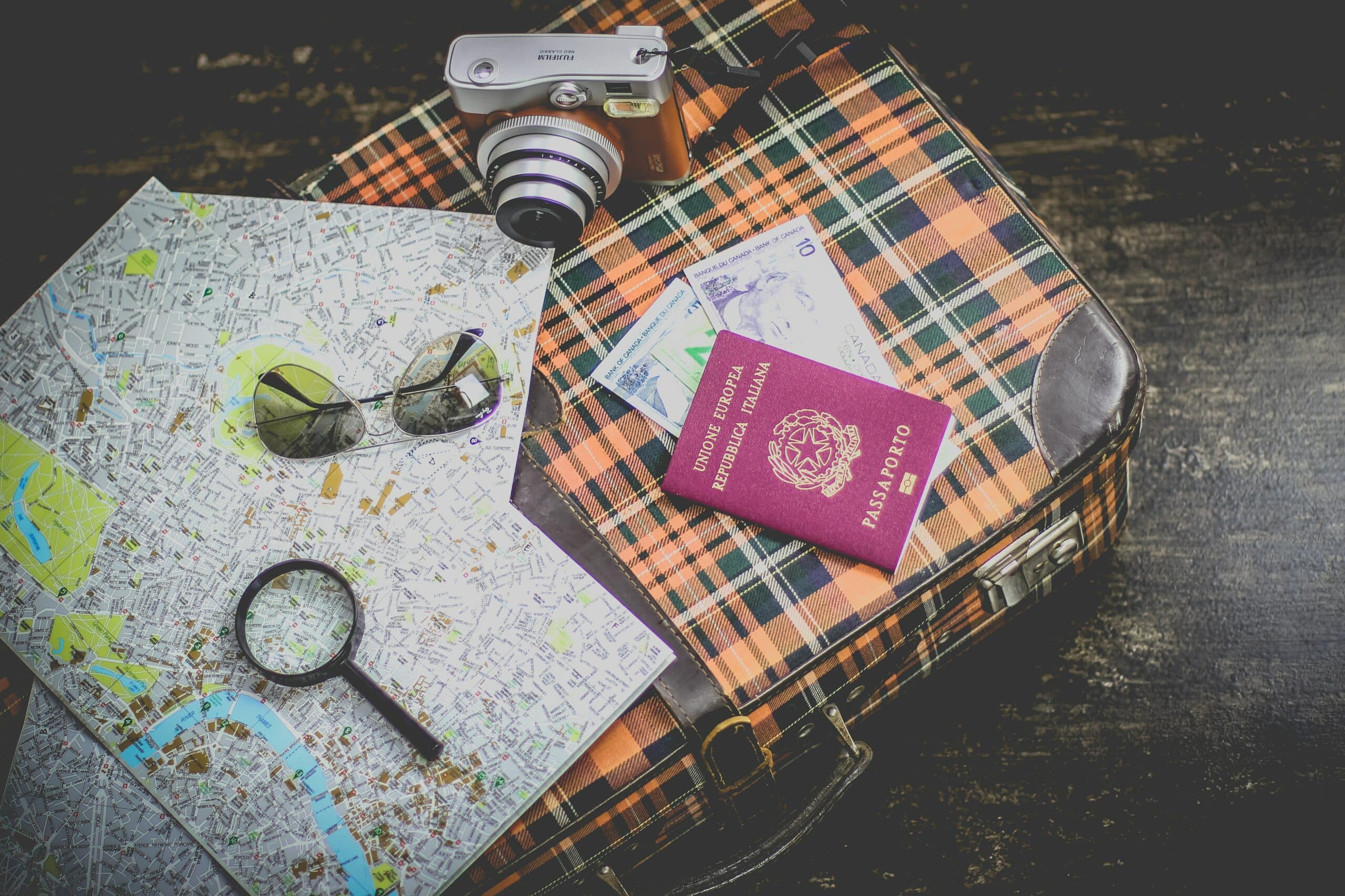 Foto de mala, passaporte, óculos de sul, lupa e câmera fotográfica para ilustrar post de cupom de desconto seguro viagem