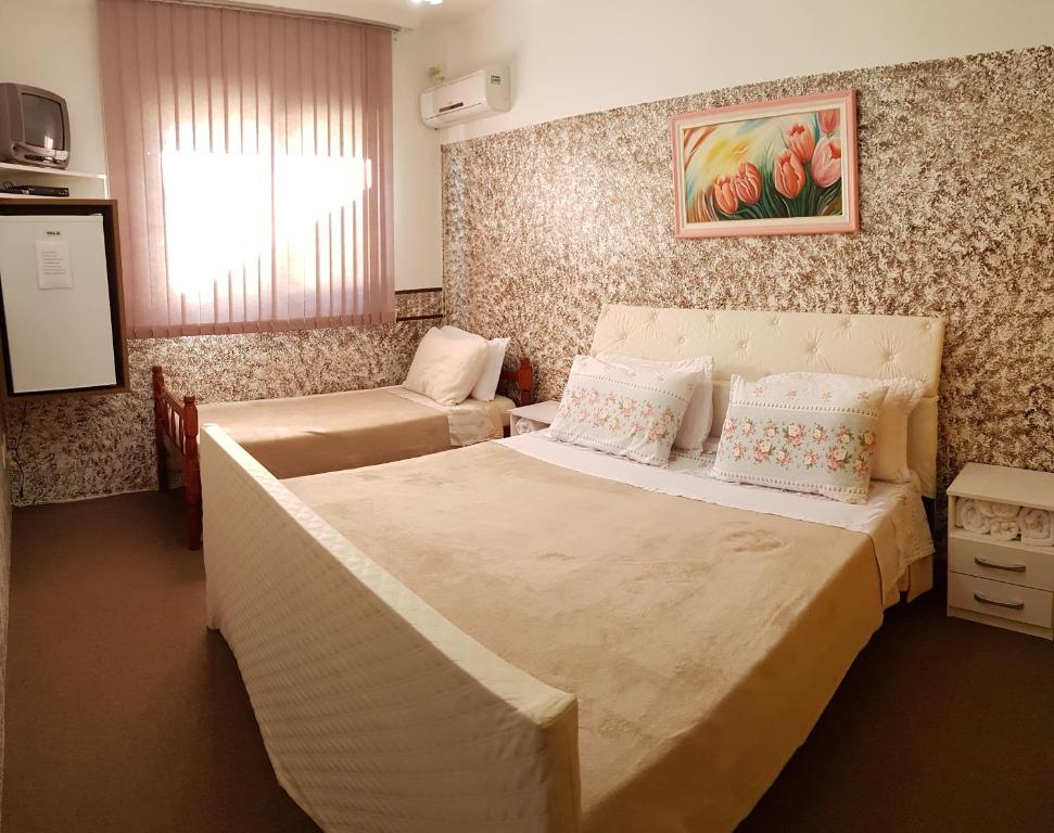 Quarto da ousada Lugama em Bento Gonçalves com cama de casal, cama de solteiro, mesa de cabeceira, ar-condicionado, TV e frigobar no canto