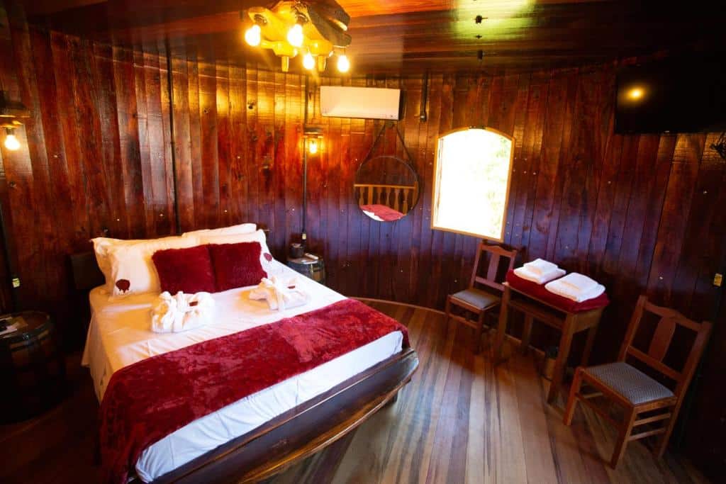 Quarto com as paredes arredondadas na Pousada Botte di Vino, dica de onde ficar no Vale dos Vinhedos, onde se vê a cama, um ar-condicionado, um espelho redondo, uma mesa com toalhas e duas cadeiras