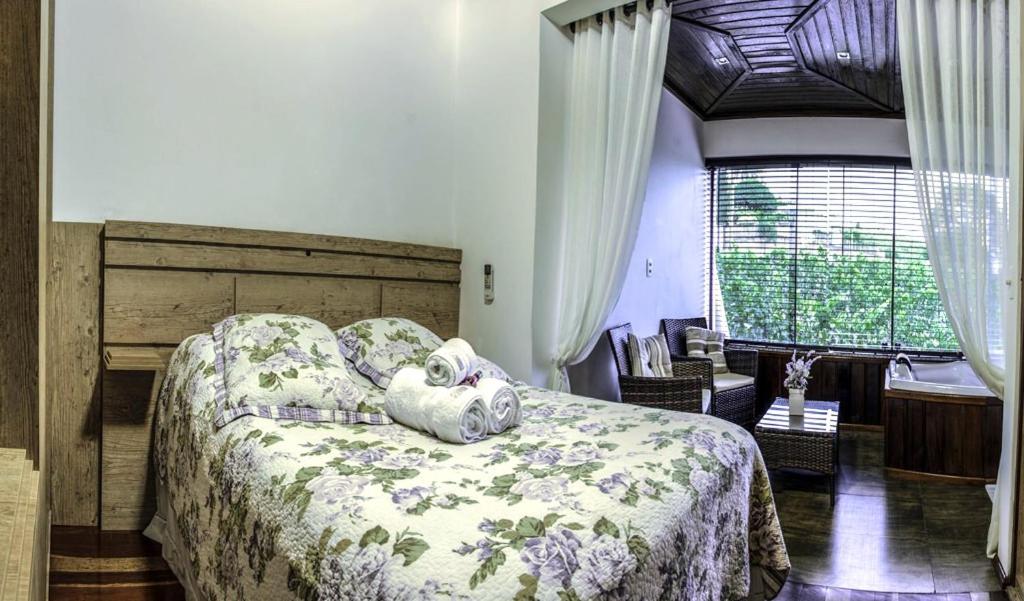 quarto da Vinícola & Pousada Terragnolo com cama de casal em primeiro plano, com roupa de cama florida, e ao fundo poltronas e hidro