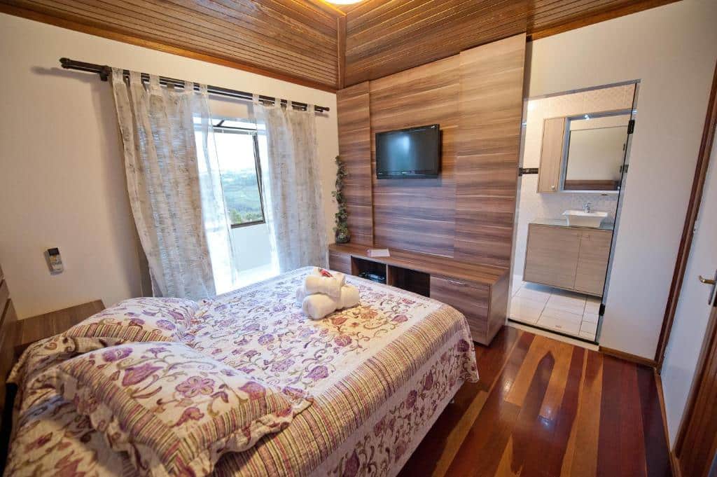 Quarto da Vinícola & Pousada Terragnolo em Bento Gonçalves com cama de casal e TV, além de porta do banheiro aberta