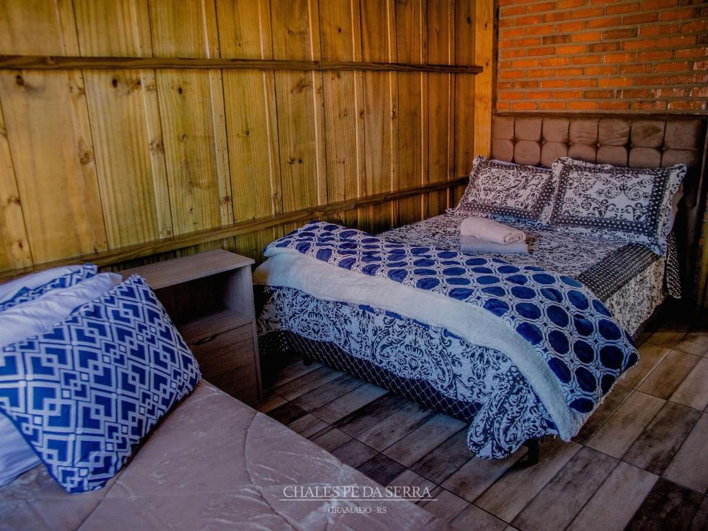 Um quarto nos Chalés Pé da Serra em Gramado com uma cama de casal, uma cama de solteiro, roupa de cama estampada, paredes de madeira e uma parede de tijolos, para representar chalés românticos no Rio Grande do Sul.