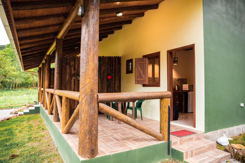 Alpendre de madeira com corrimão, duas cadeiras verdes e uma pequena mesa do lado de fora de uma casa com paredes verdes e amarelas, onde está localizado o Ninho das Águias Cabana em Nova Petrópolis.