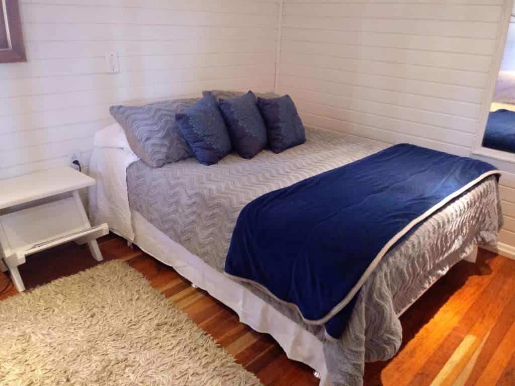 quarto do Chalé Pinheiros com uma cama de casal arrumado com cobertores cinza e mantas azuis escuras.