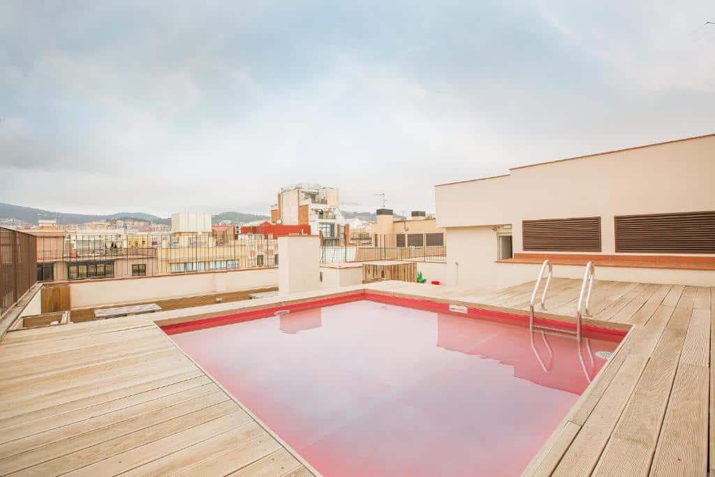 Piscina rosada no terraço do Yeah Barcelona Hostel, uma das recomendações de hostels em Barcelona. É possível ver a cidade da beira da cobertura.