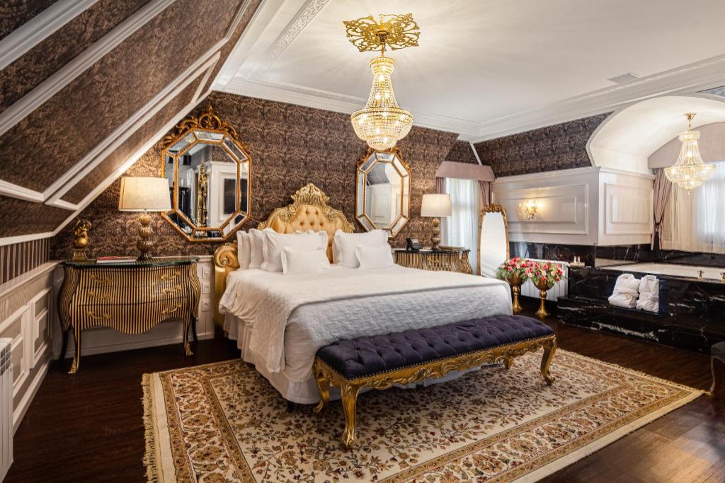 Suíte do Hotel Colline de France em Gramado com mobílias luxuosas em tons dourados, paredes com texturas escuras e um lustre de cristal pendurado no teto.