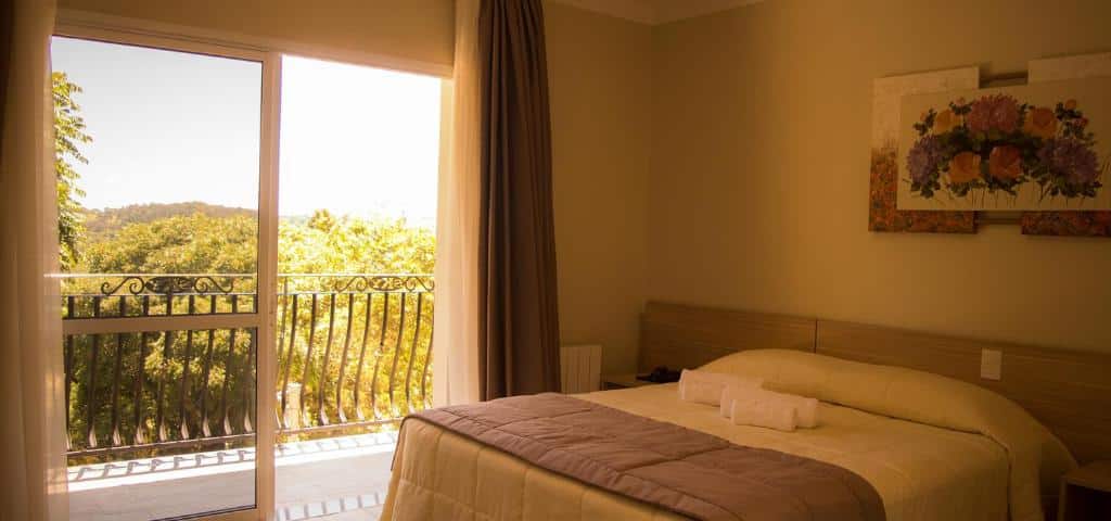 quarto do Sky Serra Hotel com uma cama de casal no lado direito e uma sacada com a porta aberta no lado esquerdo.