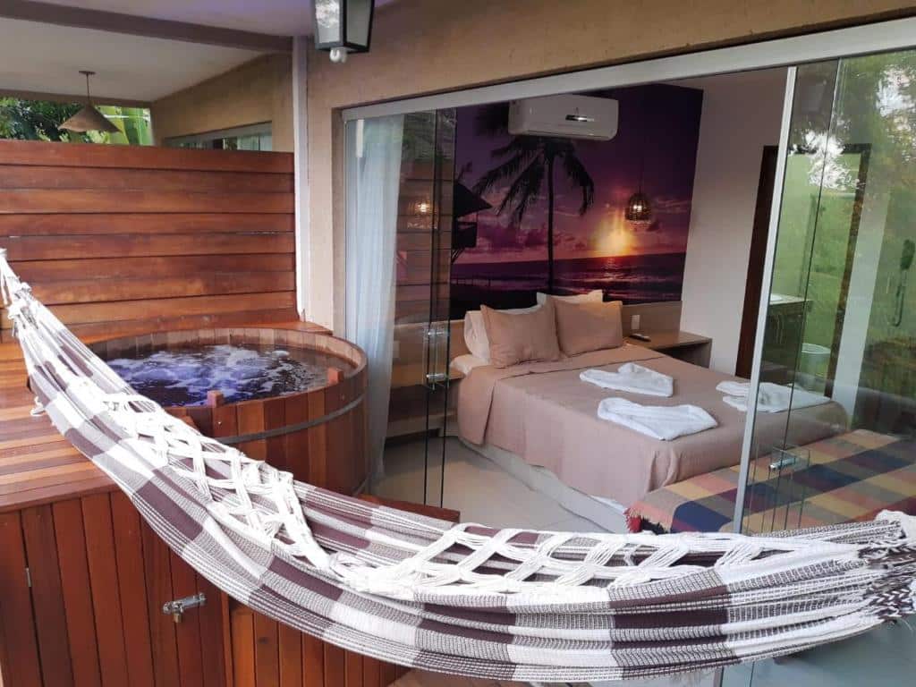 suíte do Villas do Pratagy com uma banheira de hidromassagem na varanda ao lado de uma rede e a cama de casal ao fundo