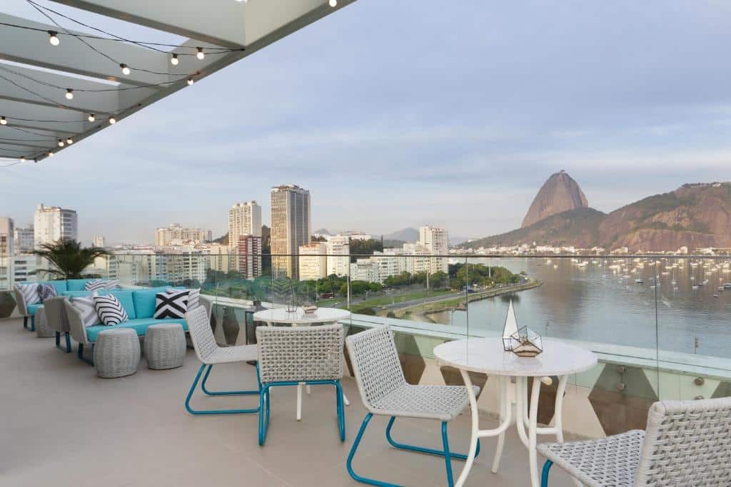 hotel Yoo2 Rio de Janeiro by Intercity com vista privilegiada para a cidade da varanda do local, onde há mesas com cadeiras ou sofás com estofado cor turquesa