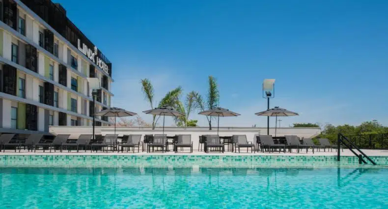 Piscina externa com água azul clara, espreguiçadeiras e guarda-sóis sob um céu claro no Linx Galeão, um dos hotéis perto do Aeroporto do Galeão.