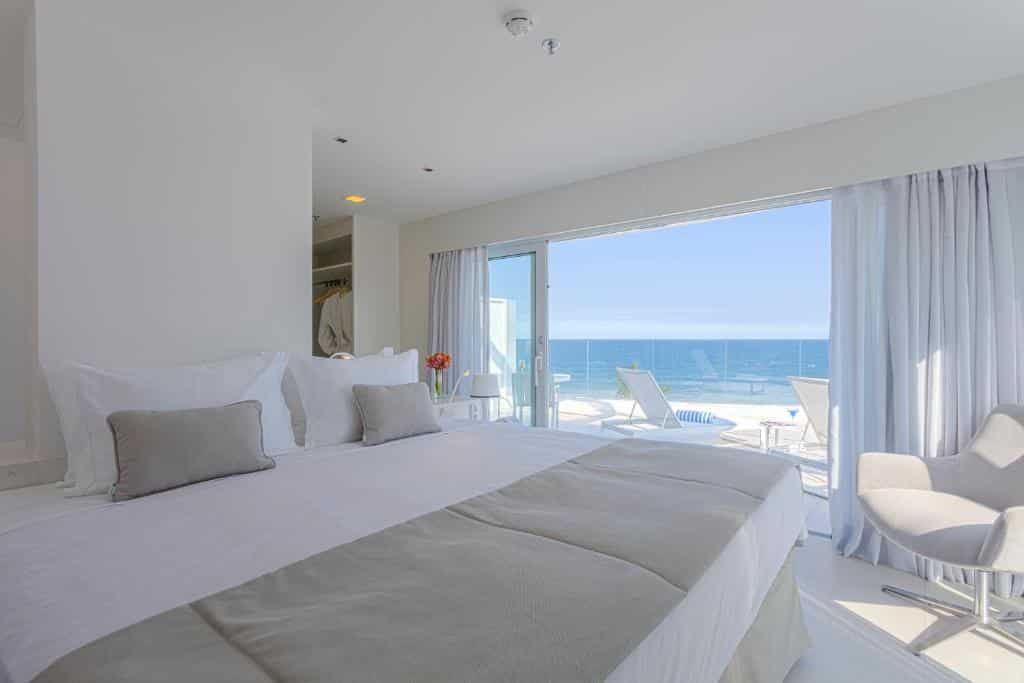 quarto do CDesign com cama super grande, varanda espaçosa com cortina e espreguiçadeiras, além de vista para o mar