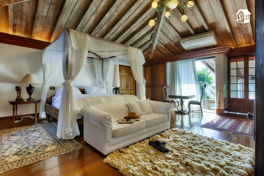 quarto do Le Chateaux Joá Boutique Hotel, com cama de casal envolta por dossel, tapetes, ar condicionado, mesas de cabeceira com abajures e chão e teto de madeira